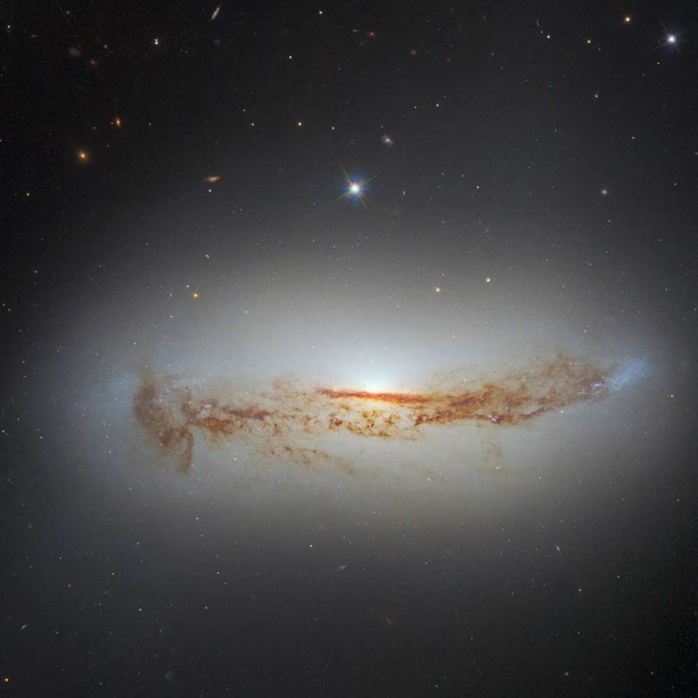 Hubble Space Telescope image of NGC 7172, a dusty edge-on spiral galaxy with a glowing central bulge and prominent dark dust lane obscuring parts of the stellar disk.