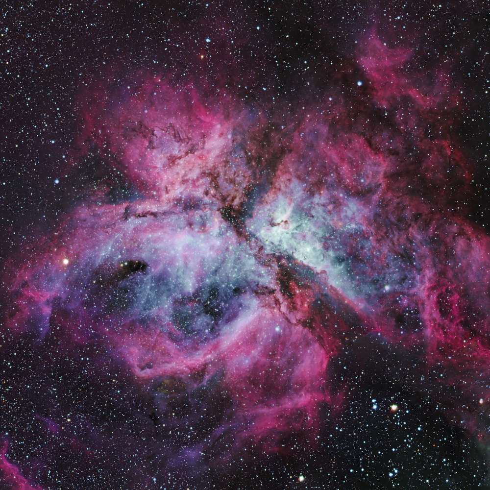 High-resolution image of the Carina Nebula showing glowing clouds of ionized gas and dark dust lanes in a massive star-forming region of the Milky Way.