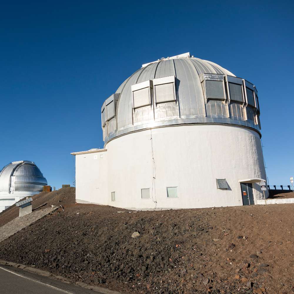 White and silver domed infrared telescope observatory located on a volcanic summit under clear blue sky.