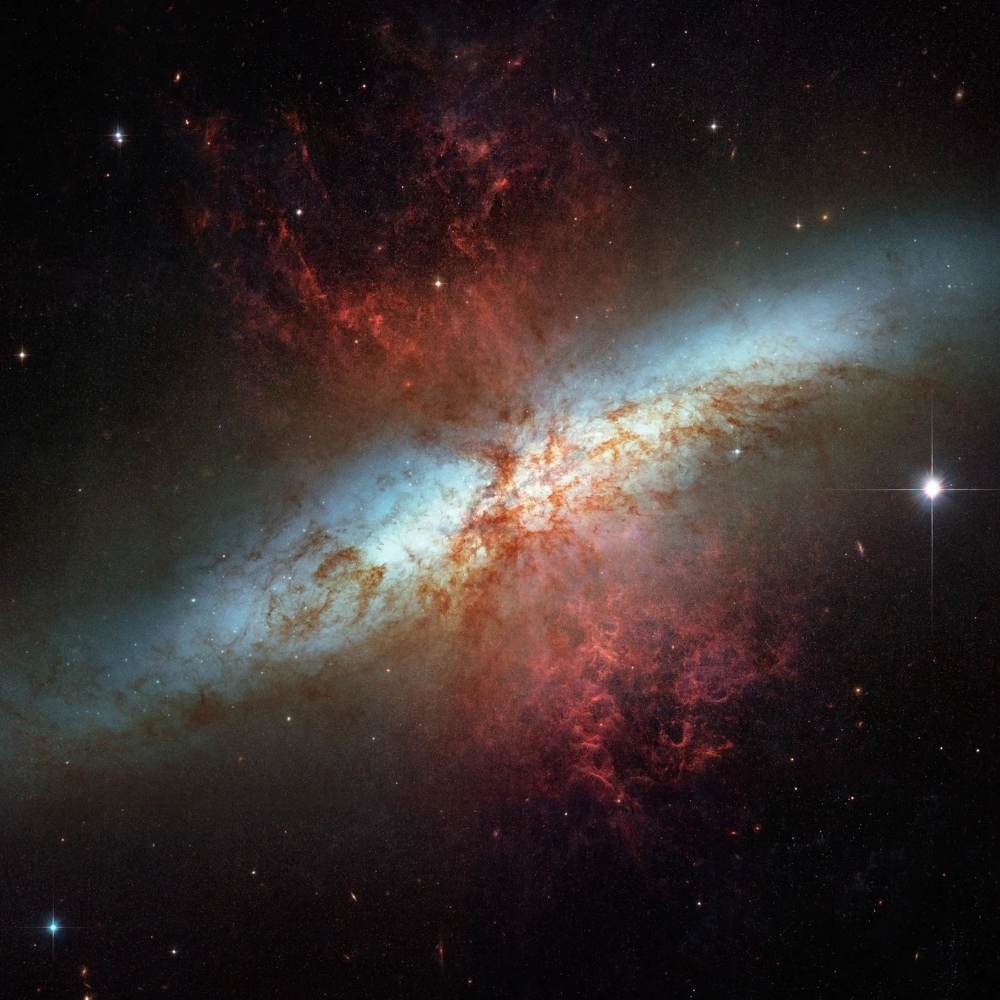 Hubble image of the Cigar Galaxy (Messier 82) showing bright starburst regions and red gas outflows caused by intense stellar winds.