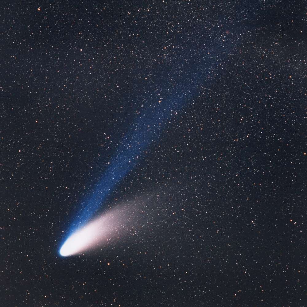 Hale-Bopp comet with a bright nucleus and long blue ion tail and white dust tail, visible against a dense star field during its historic 1997 apparition.