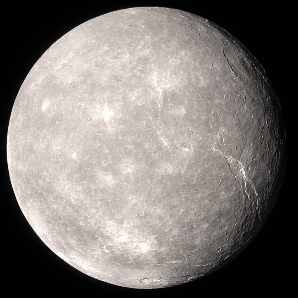 Titania, the largest moon of Uranus, showing an icy surface with impact craters, fault lines, and large canyons revealed by Voyager 2 imagery.